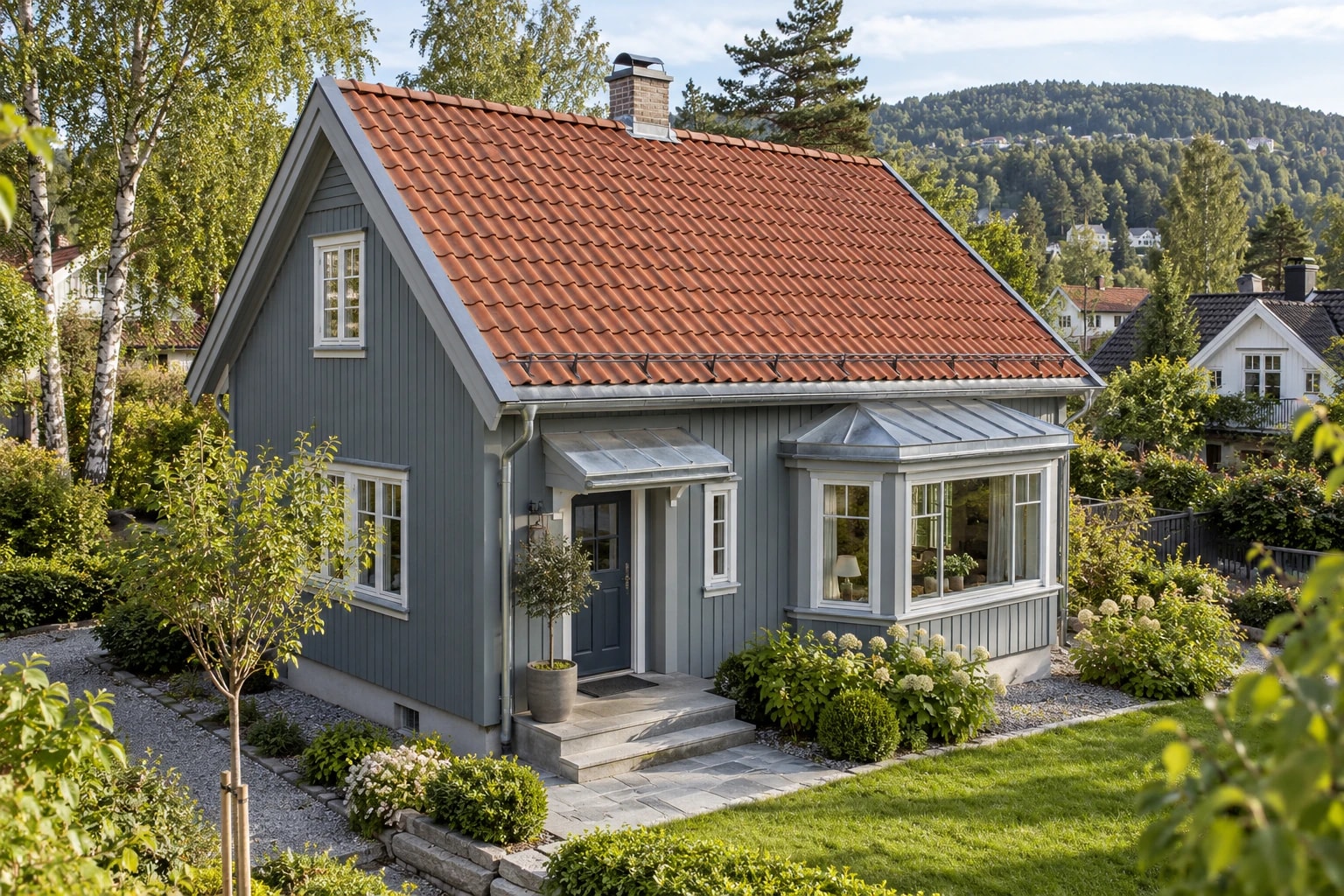Blågrå villa med rødt tegltak og tilpassede metallbeslag ved et karnapp.