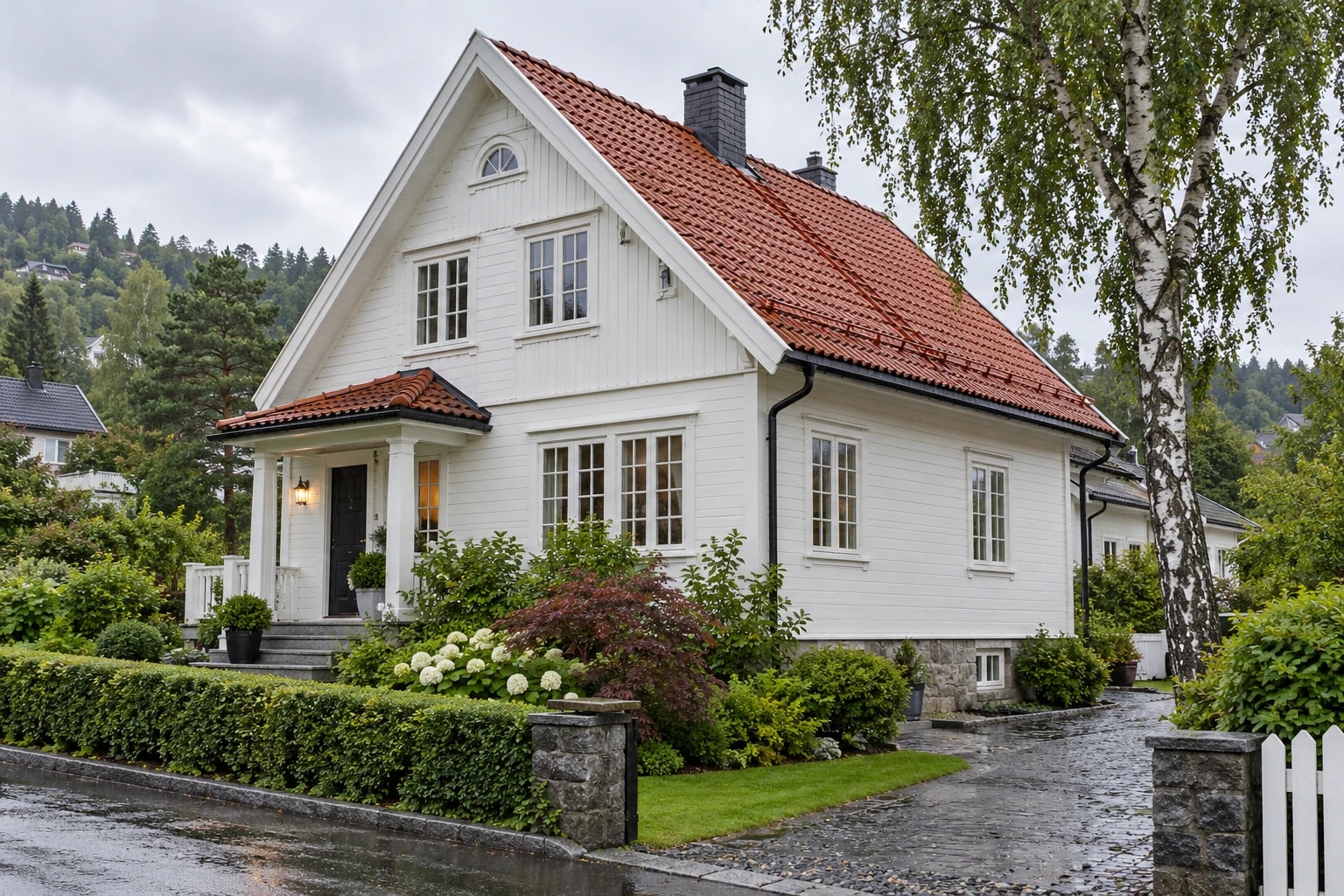 Hvit trevilla med røde takstein og svarte takrenner i vått vær.